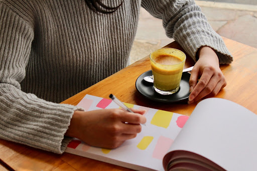 A person sitting down with a coffee ready to start writing on her notepad.