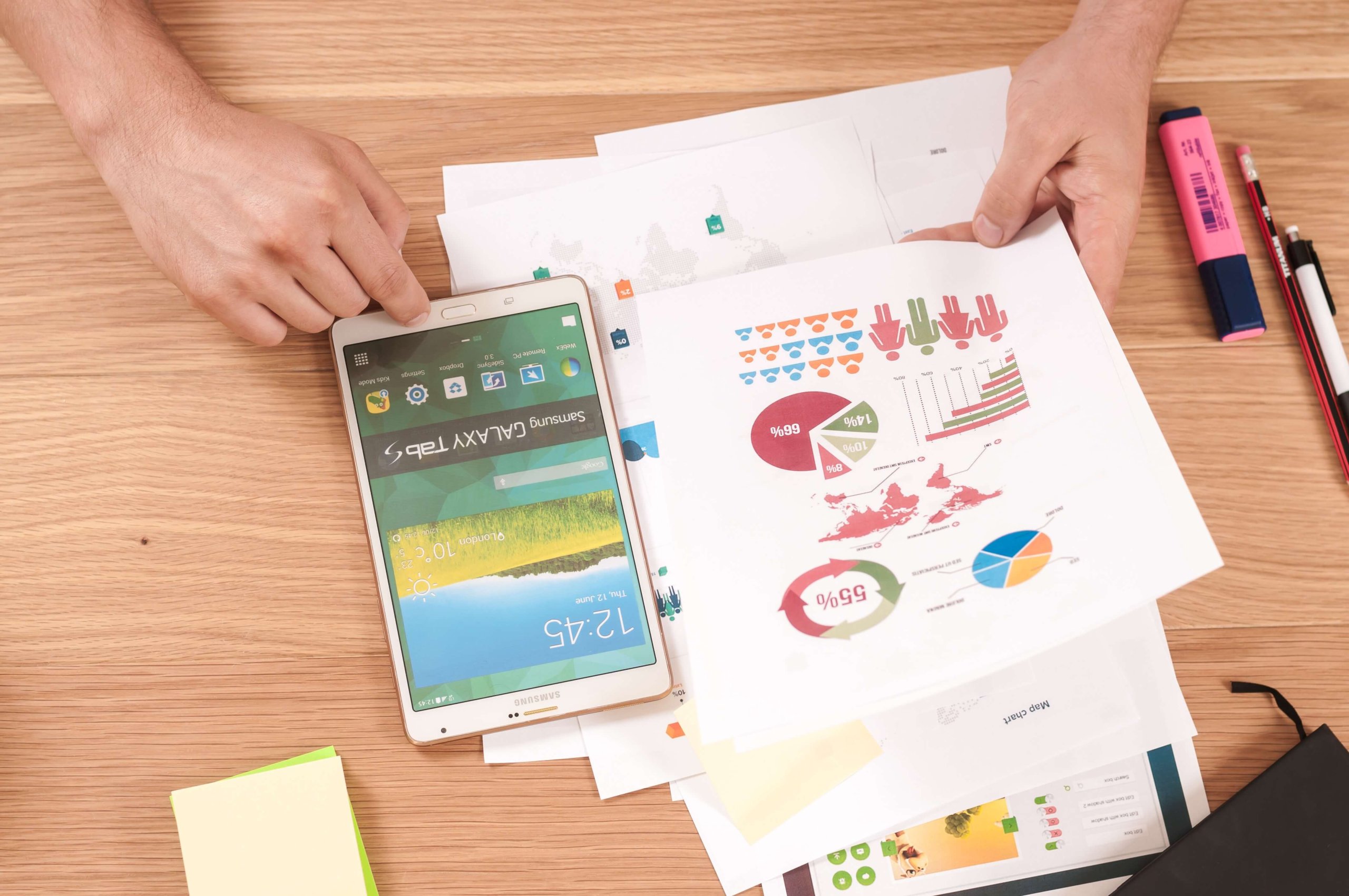 Someone looking at various graphs on paper whilst at a desk. Using phone at the same time