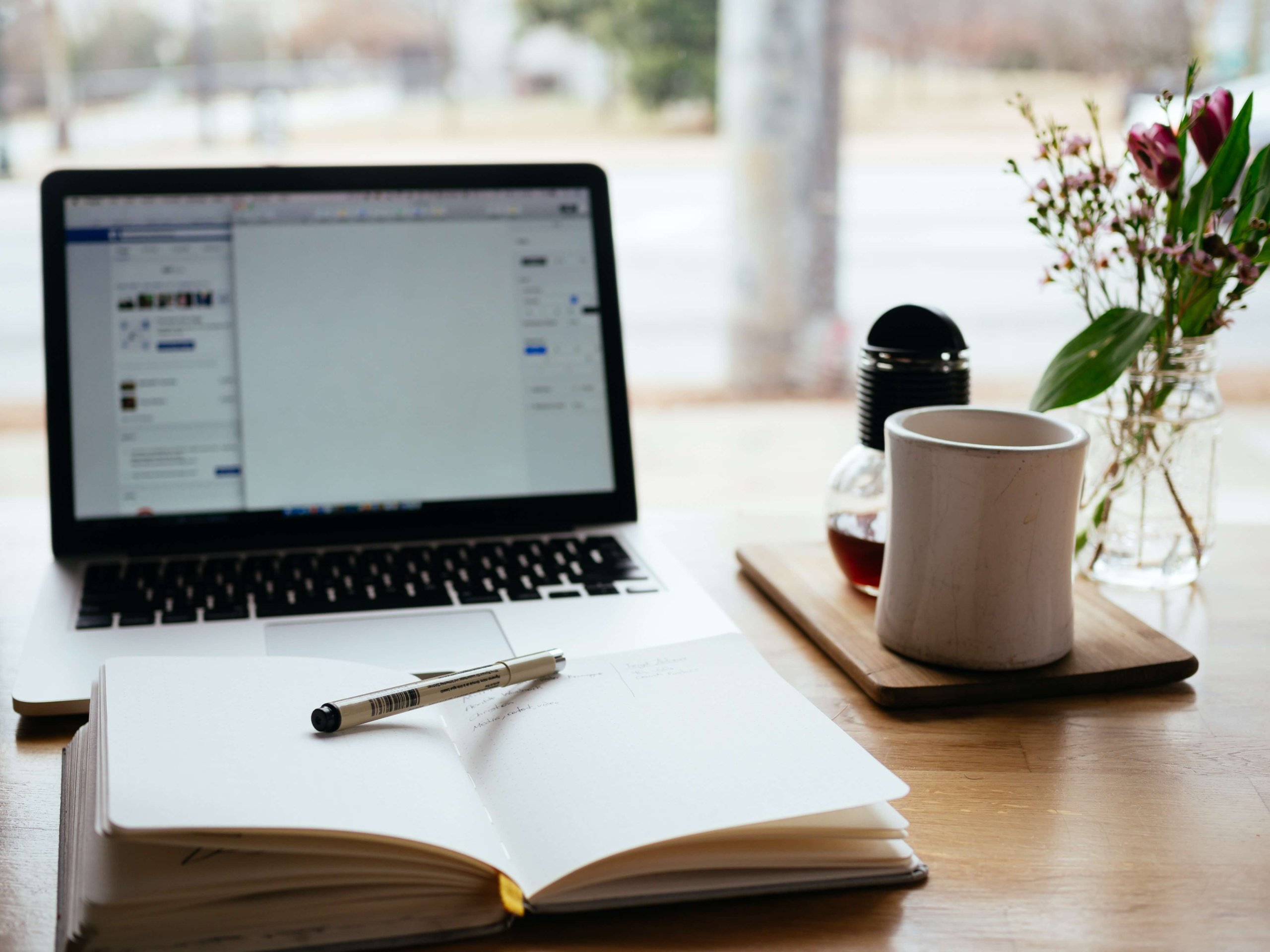 Open laptop with open book in front. Coffee cup on side of desk